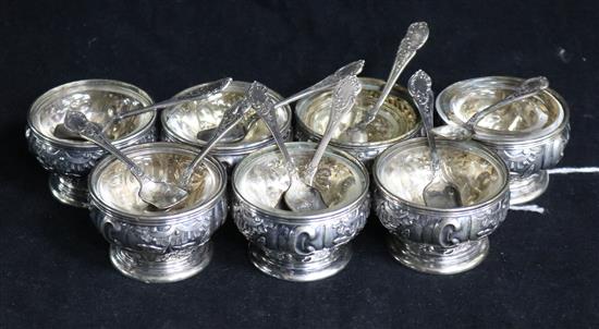 A set of seven German circular silver pedestal salts, embossed with scrolls and foliage (replacement liners) and nine spoons